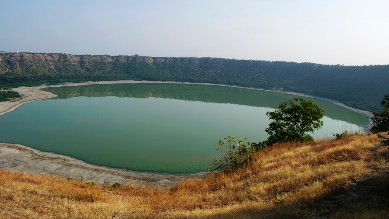 7. Lonar Lake, Maharashtra Formed by a meteor strike over 50,000 years ago, Lonar Lake is one of only four known hyper-velocity impact crater lakes in basaltic rock. Encircled by forests and ancient temples, its green-hued waters sit quietly within a perfectly round basin—a natural marvel tinged with geological mystique. (Image: Canva)