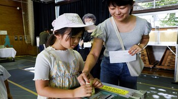 A girl tries to cast her mother's ballot with her help during the Upper House election at a polling station in Tokyo, Japan July 20, 2025. REUTERS/Manami Yamada