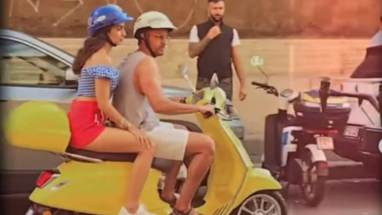 On a bright yellow Vespa, bringing European street charm to the scene. The perfect blend of cinematic romance and holiday feels.