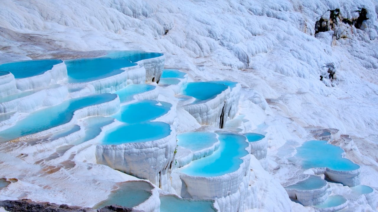 11. Pamukkale, Turkey Pamukkale’s “cotton castle” terraces, formed by calcium-rich thermal waters, cascade down the hillside in shimmering white pools. The mineral-rich water, warm and inviting, has drawn visitors since Roman times. At sunset, the pools glow pink and gold, creating a scene so magical it feels like stepping into a fairytale realm. (Image: Canva)