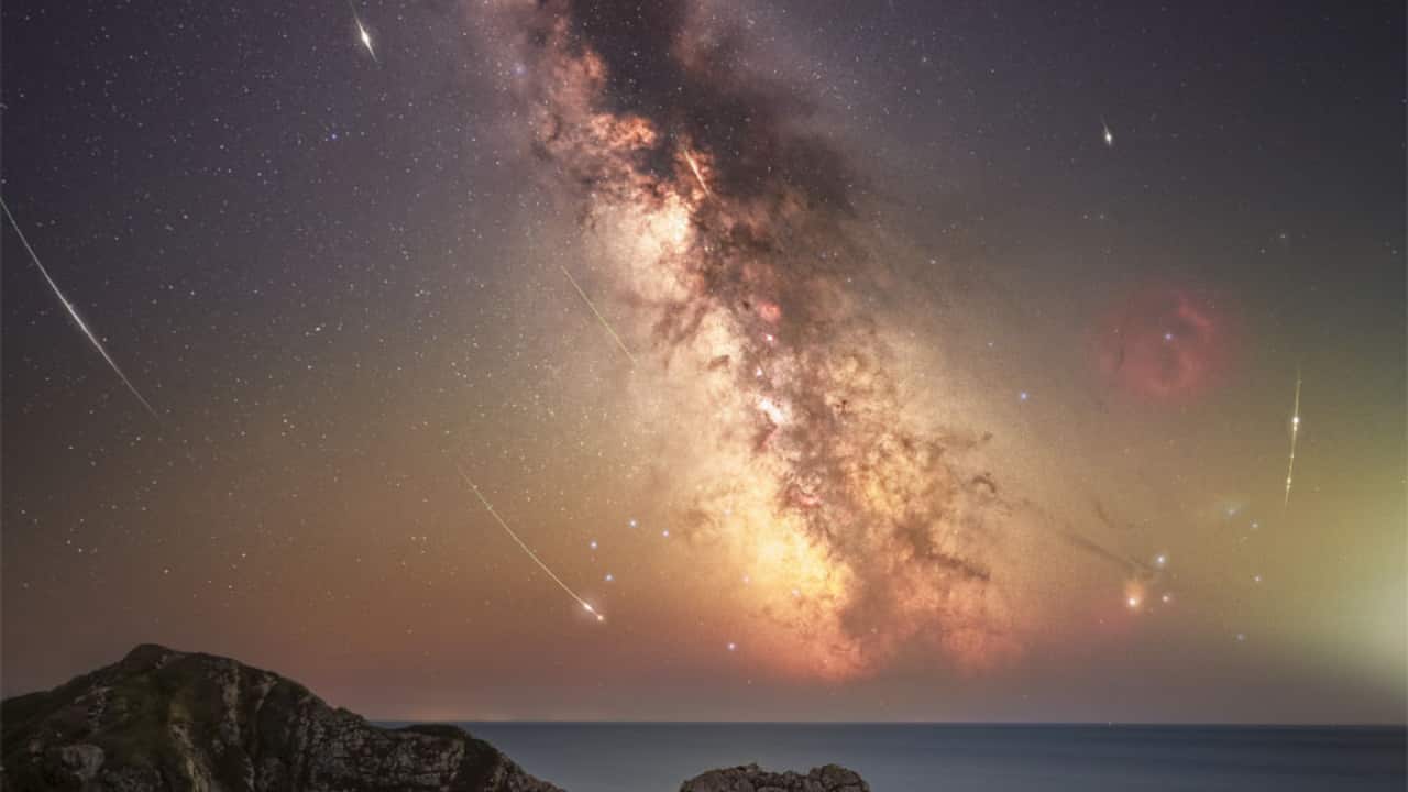 Perseid Meteors from Durdle Door: Perseid meteors streak across Dorset’s Durdle Door sky, captured in a composite image where curved arcs point to Perseus, with the Milky Way glowing behind. (Image: NASA)