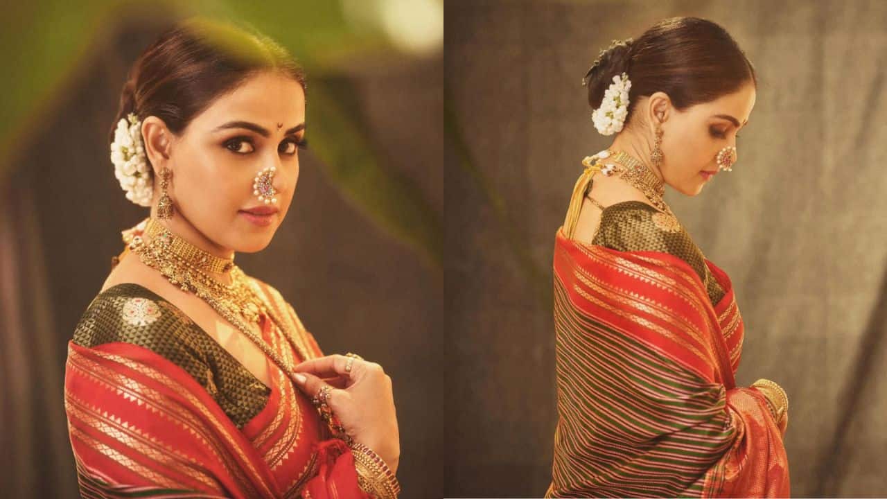 Genelia Deshmukh Genelia Deshmukh looks stunning in a traditional outfit for Ganpati celebrations. She wears a beautiful red and green saree with intricate golden work, paired with a matching blouse. The rich colors and design make the ensemble festive and elegant. Her jewelry is traditional, featuring a gold choker, intricate nose ring, and earrings. Her hair is styled in a neat bun adorned with white flowers, completing the look with grace and charm, perfect for the occasion.