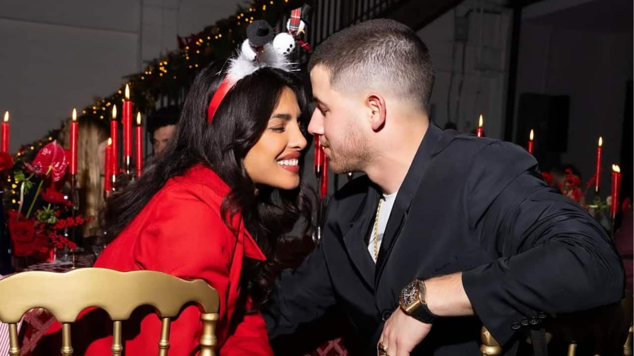 The Christmas Moment with Priyanka and Nick  At a Christmas celebration, Priyanka Chopra and Nick Jonas share a happy, private moment. Nick leans in affectionately as Priyanka, wearing a red outfit and a playful snowman headband, beams amid the festive décor and warm lights. The warmth and charm of the holidays are radiated by their smiles and intimacy.