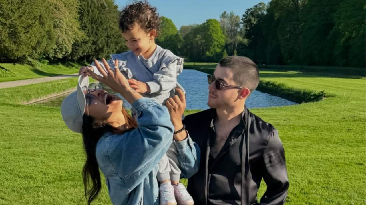 Sunshine and Joy  Nick Jonas watches with a warm smile as Priyanka Chopra joyfully lifts her daughter Malti outside. The family exudes joy and unity as they are surrounded by sunshine and lush greenery. It's an open celebration of their love, humor, and the priceless relationship they have as parents.