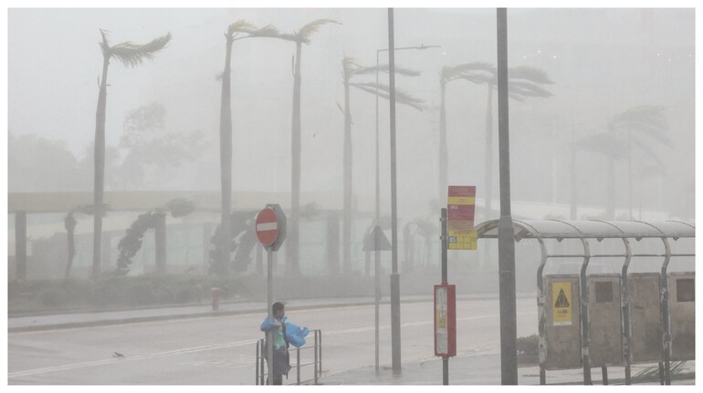 A woman clings to a traffic sign to maintain balance against strong winds from Super Typhoon Ragasa in Hong Kong. (Courtesy: Reuters photo)
