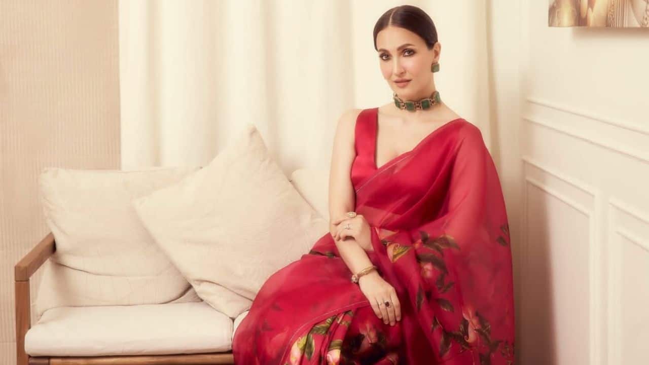 Give me red Elli's cherry red saree is an example that red is always right for a celebration. She chose a sleeveless blouse that added a modern touch to a semi-sheer drape with multicolored floral accents. Give me red Elli's cherry red saree is an example that red is always right for a celebration. She chose a sleeveless blouse that added a modern touch to a semi-sheer drape with multicolored floral accents.