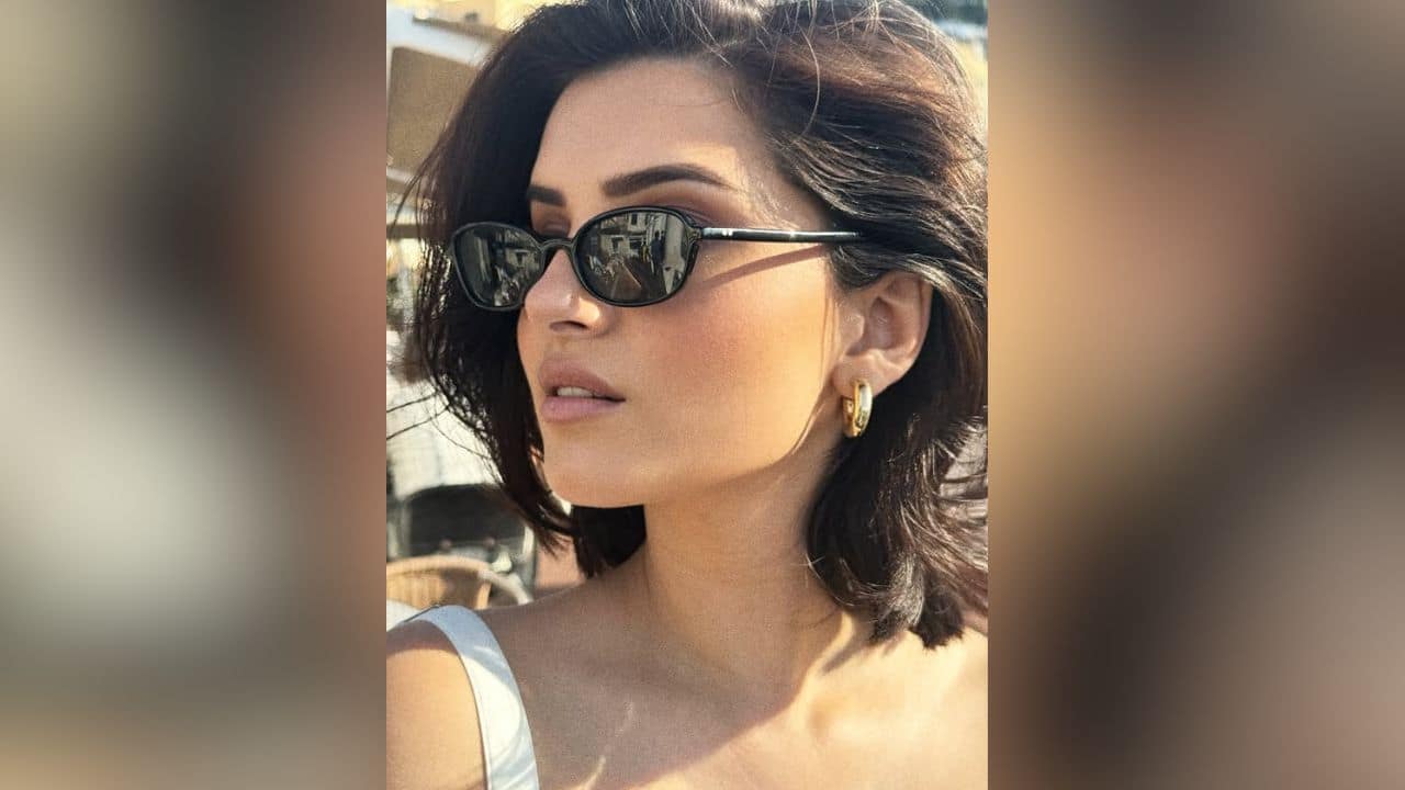 9. This elegant close-up captures Tara Sutaria basking in the bright sunlight outdoors. Her chic look features classic black oval sunglasses and simple gold hoop earrings, beautifully framing her short dark hair and natural makeup.
