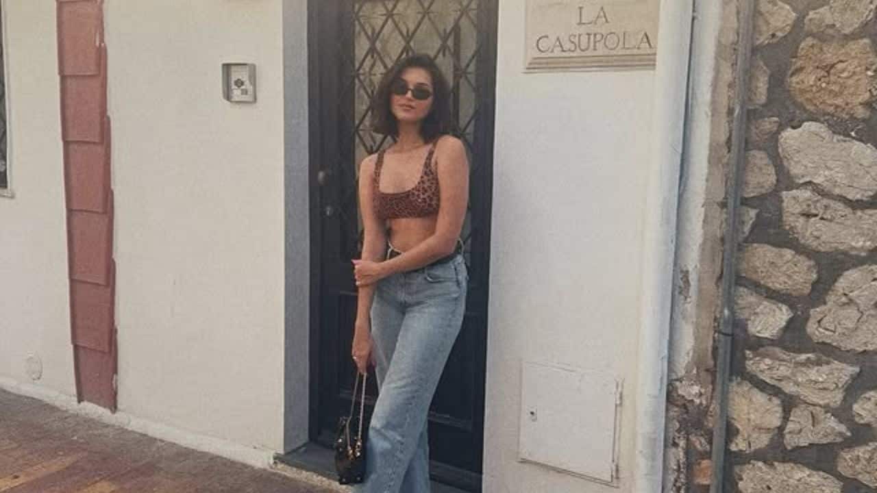 In this picture, Tara Sutaria poses outside a white building with a sign reading &quot;LA CASUPOLA&quot; during their vacation in Italy. She is wearing a leopard-print crop top, light jeans, and white sneakers in the bright sunlight.