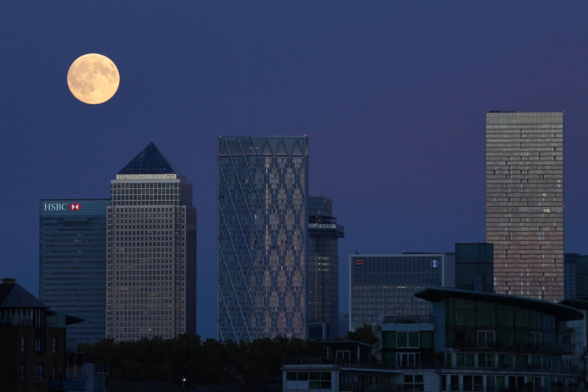 The Harvest Supermoon ascends above Canary Wharf in London on Monday, October 6, 2025. (Image: AP Photo/Kin Cheung)