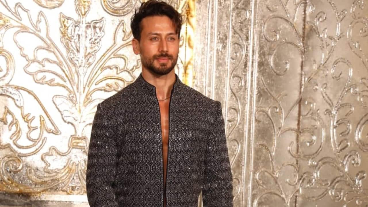 Tiger Shroff Tiger Shroff looked dapper in a contemporary, shimmering traditional kurta paired with black pants. The actor flaunted his bare chest underneath as he kept his high-neck style kurta open. He completed his look with a thin necklace.