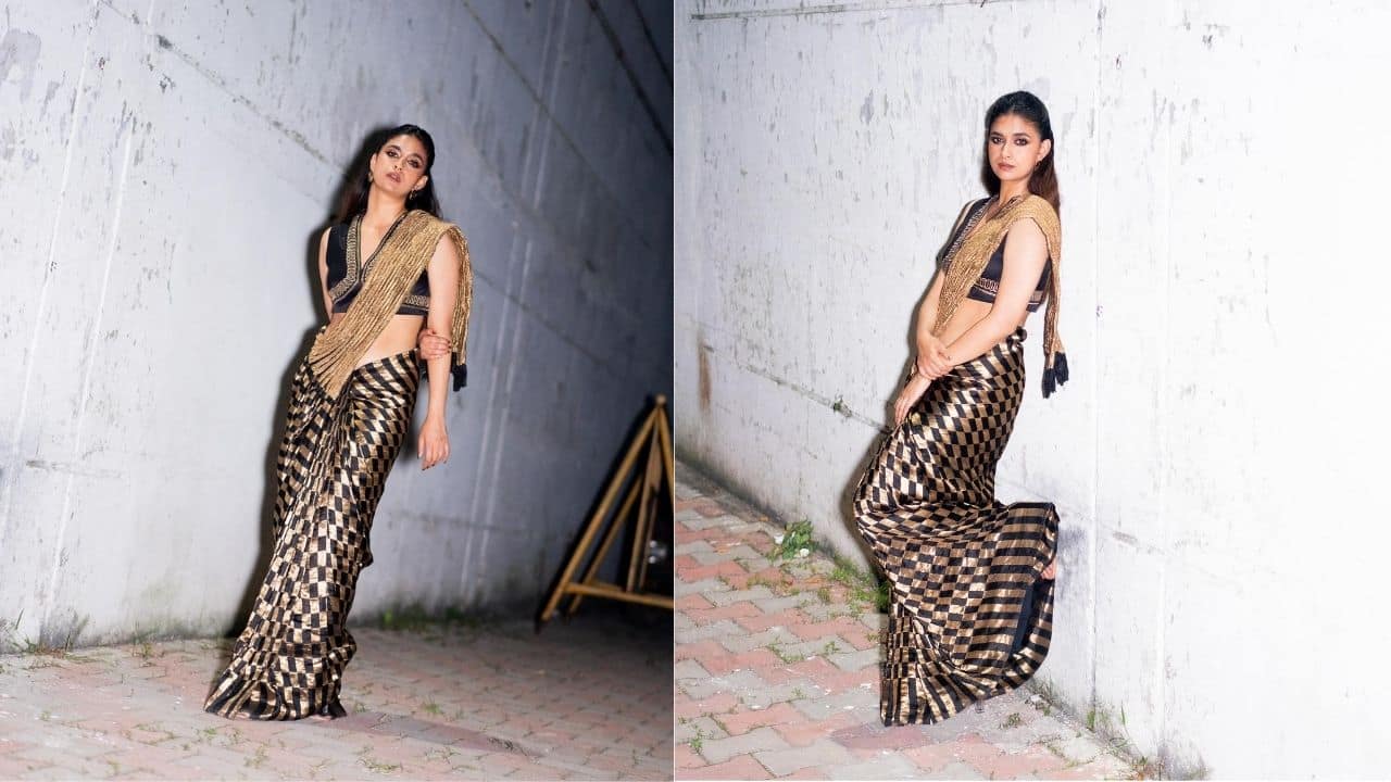 Golden Hues, Royal Vibes In a glowing golden silk saree with a shimmering golden pallu and black and gold checked borders at the bottom, embrace the festive spirit like Keerthy Suresh. She let elegance shine naturally by wearing it with a black V-neck blouse and few accessories.