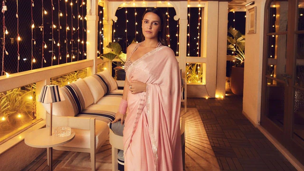 Neha Dhupia For Diwali, Neha Dhupia showed a mix of modern glamour and tradition by wearing a pastel pink saree and a striking blouse with mirror work, both of which were created by Manish Malhotra. Fans dubbed her &quot;Barbie-core&quot; moment because of the way the stunning, heavily decorated sleeveless blouse with a deep V-neckline perfectly matched the soft, flowing fabric of the saree. She exuded elegance and festive cheer by accessorizing with matching pink bangles and wearing minimal makeup to complete the look.