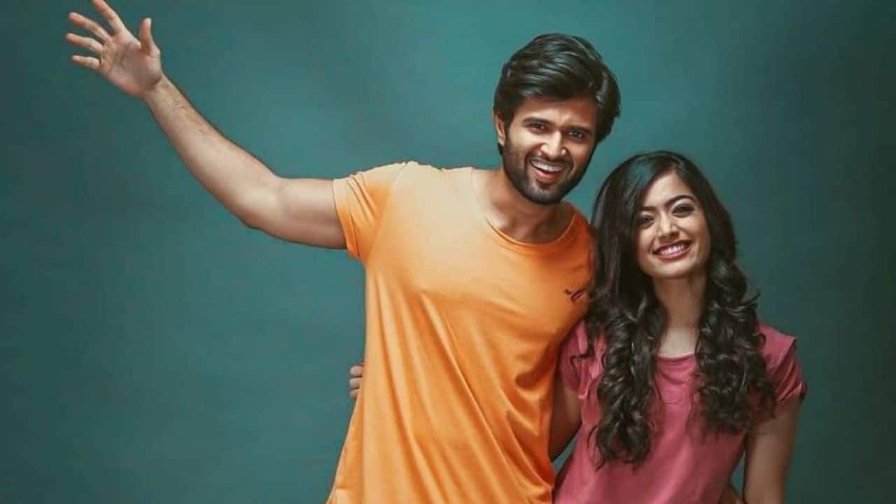 Playful Partners in Crime Vijay and Rashmika's casual, comfortable energy shines through as they share a warm embrace and playful wave. His vibrant orange tee complements her sweet smile, highlighting their fun, easygoing chemistry that their fans adore both on-screen and off.