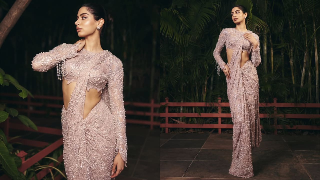 <strong>Sequin Embellished Saree</strong><br />Khushi looks ethereal in this incredibly chic and contemporary classic saree. The entire ensemble is made from sheer fabric that has been tinted blush or mauve and is entirely covered in tiny, painstakingly applied sequins, beads, or tiny pearls, giving it a shimmering texture. The modern, structured drape of the saree draws attention to the movement and glimmer of the fabric.