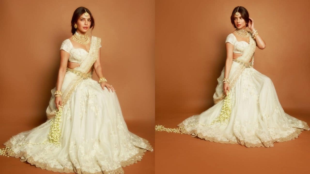 Sitting elegantly in a flowing ivory lehenga with intricate embroidery and shimmering gold accents, Priyanka Chopra is the epitome of grace and tradition. Her regal aura is enhanced by the delicate craftsmanship of the ensemble and her lavish jewellery, which includes layered bangles, a maang tikka, and a heavy choker. Her dupatta falls perfectly symmetrical when draped elegantly, and the traditional South Indian touch is added by the jasmine flower strands. Priyanka's Varanasi appearance, which is ageless, divine, and rich in cultural splendour, is masterfully brought together in this final frame.