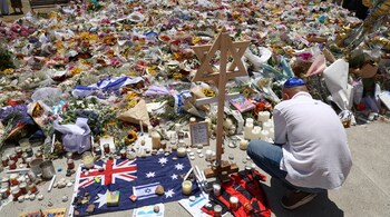 A mourner lights candles as people gather around floral tributes outside Bondi Pavilion in Sydney on December 17, 2025, to honour victims of the Bondi Beach shooting. (Photo by DAVID GRAY / AFP)