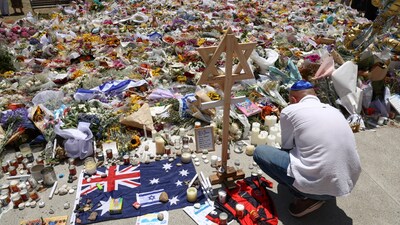 A mourner lights candles as people gather around floral tributes outside Bondi Pavilion in Sydney on December 17, 2025, to honour victims of the Bondi Beach shooting. (Photo by DAVID GRAY / AFP)