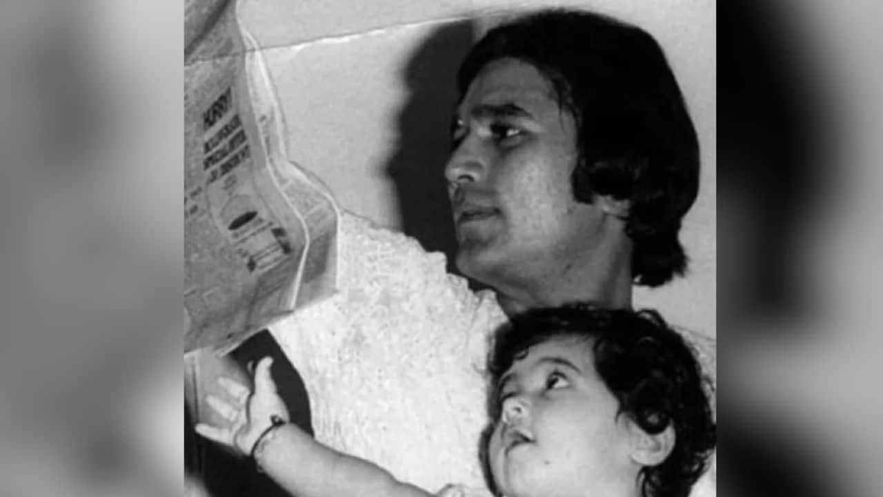 This photograph captures a quiet, intimate moment between Rajesh Khanna and his young daughter Twinkle Khanna, steeped in everyday warmth. Rajesh Khanna is seen reading a newspaper while Twinkle, nestled close, looks up at him with wide-eyed curiosity and trust.