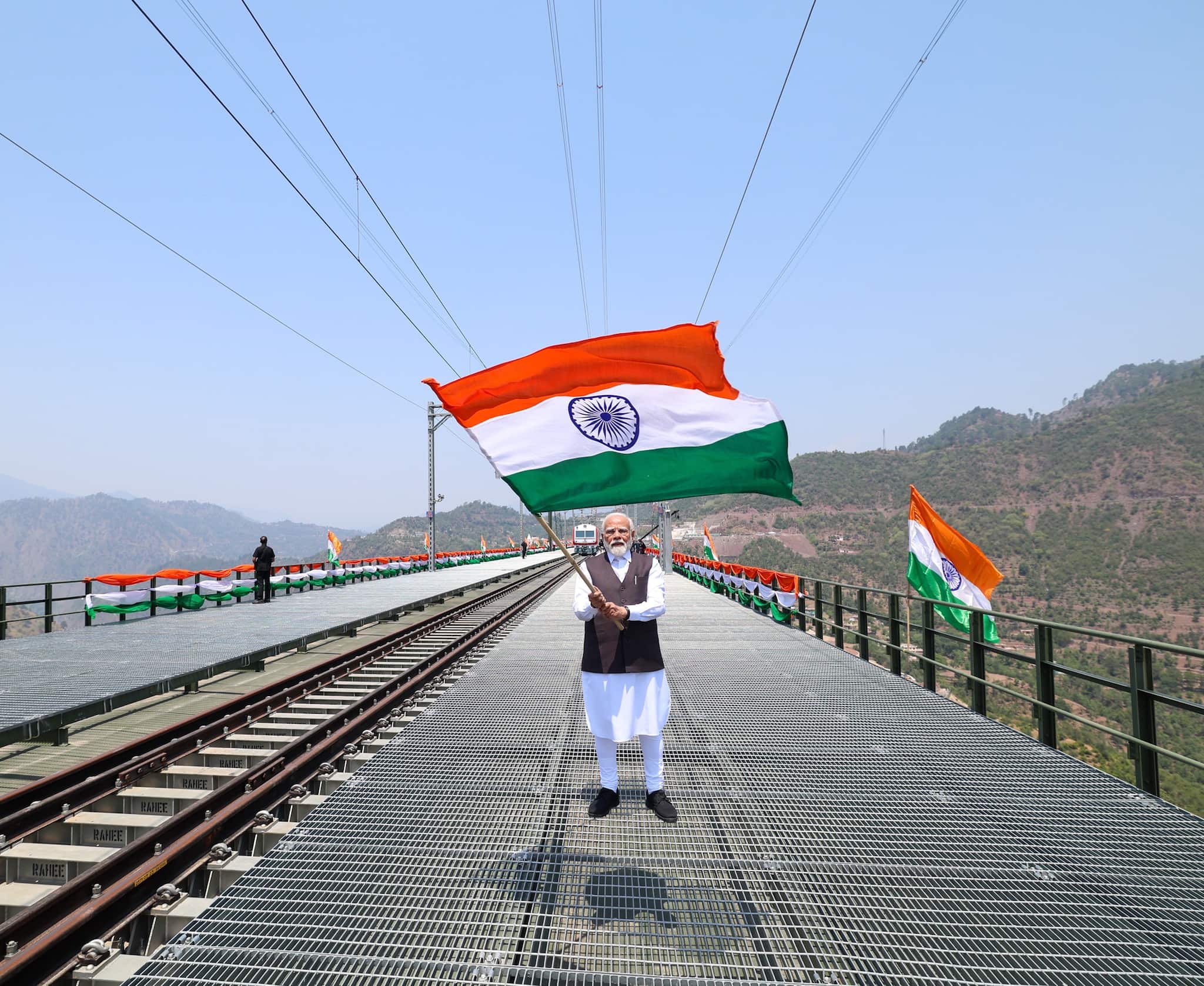 PM Modi waves the national flag as he visits the Chenab bridge, in Jammu and Kashmir. (Image: narendramodi.in)