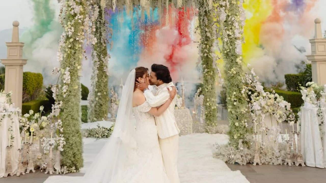 The "I Do" Moment The couple shared a romantic kiss under a lush floral archway. The moment was made even more cinematic by a background of colourful smoke cannons (Holi colours), blending vibrant Indian traditions with the white wedding aesthetic.