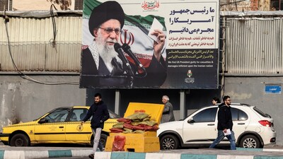 Iranians walk past a billboard showing Iranian supreme leader Ayatollah Ali Khamenei with anti-US rhetoric in Tehran on January 27, 2026. (Photo by ATTA KENARE / AFP)