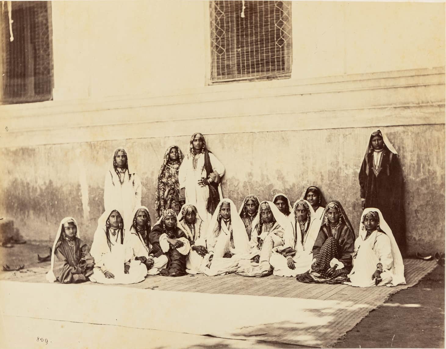 To be sure, far from being objective, the essayists explain, these photos were heavily posed. For example, if a British officer and his family were pictured in the photo with their staff, their positions and postures were carefully choreographed to highlight the prominence, power and prosperity of the British family. For the natives, a sort of SoP for making the pictures started coming together quite early on in the project. Such that when there are multiple people in a photo, they are posed sitting, standing, facing forward and in profile, to give a sense of the physical features, dress and other attributes of their race or tribe. Specific subjects in the photo were typically considered to be representative of the group. The annotations carried the presumptions and prejudices of the creator as much, if not more than the pictures themselves. But the problems with the project run deeper still. Sudeshna Guha in her essay quotes from an 1862 edition of the ‘British Journal of Photography’: “Our good friends at home constantly request us out here to take groups of the natives, but they little know what a labour it is. Only point a camera at a native, and notwithstanding his natural grace, suppleness of limb and easy carriage and bearing when taken unawares, from fear of being shot, or converted into some kind of uncouth animal by means of necromancy, he becomes, on seeing you, as rigid as the camera stand, or moves away altogether…” Some subjects simply did not want to be photographed. (Pictured here: A Group of Kashmir Females, Srinuggur; silver albumin print from wet collodion glass negative mounted on card, c. 1864; photo by Samuel Bourne courtesy DAG)