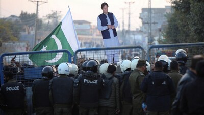 (FILES) A supporter holds a cutout of former Prime Minister of Pakistan and Leader of Pakistan Tehreek-e-Insaf (PTI) party Imran Khan, as police officers stand with the barriers, put up to stop them during a protest over concerns about their leader's health, on a road leading to Adiala jail in Rawalpindi, Pakistan, December 2, 2025. REUTERS/Stringer