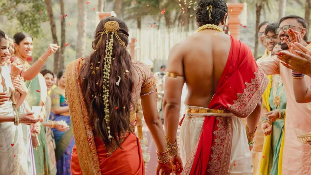 Hand in hand, Rashmika and Vijay walk forward as guests shower them with petals. Her intricately draped sari trails behind, connected visually with his red angavastram. The frame symbolizes a shared journey, tradition woven into every step they take together.