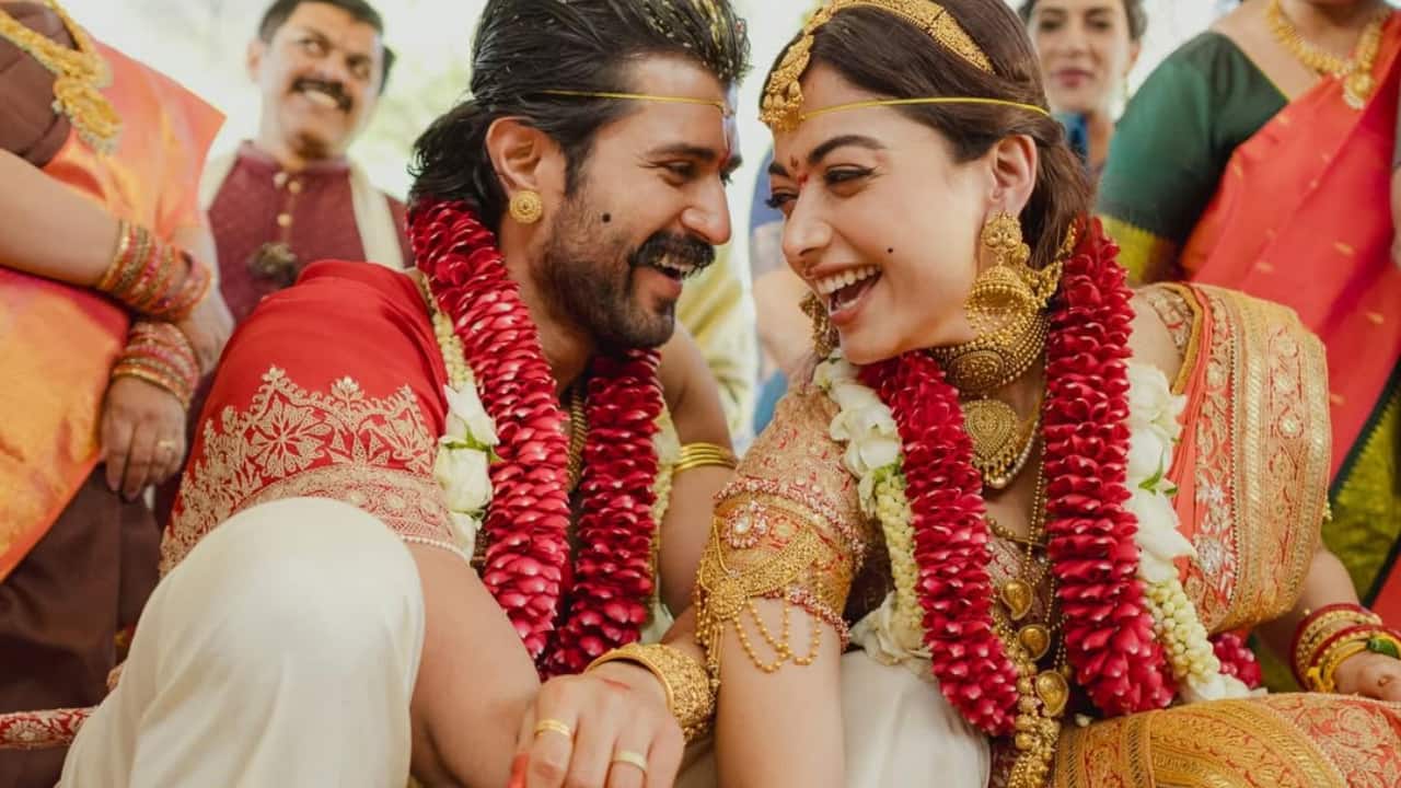 Seated side by side during a ritual, Rashmika and Vijay laugh freely, their chemistry effortless and warm. Surrounded by family, flowers and sacred elements, the moment feels candid and real. The alta on Vijay’s hands subtly stands out, blending tradition with expressive detail.