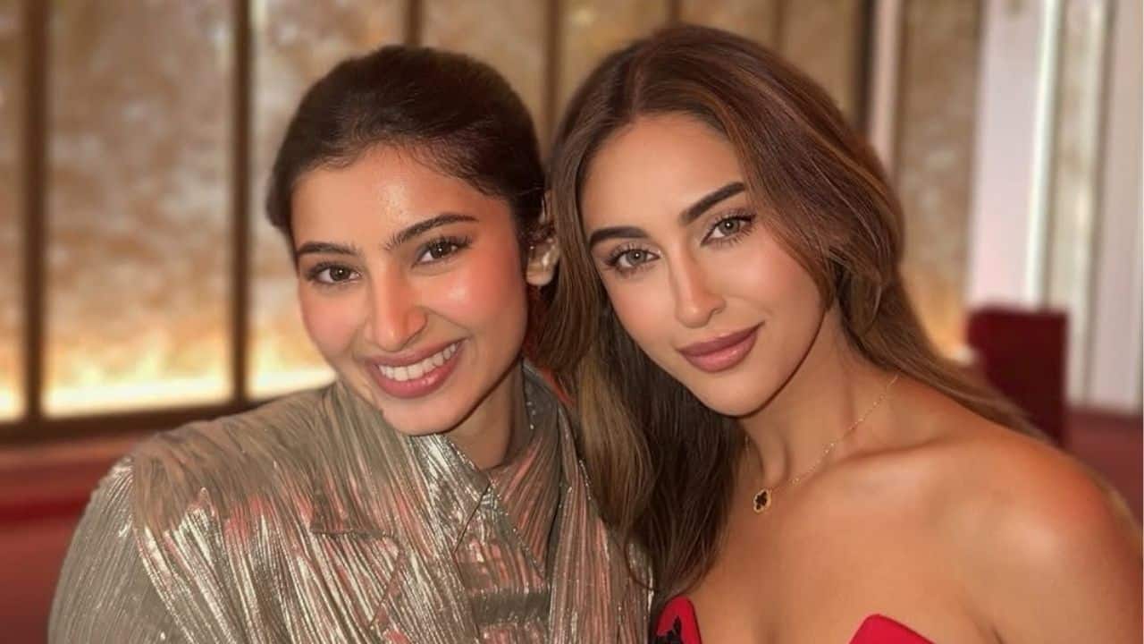 Sara Arjun and Krystle D'souza pose closely, both looking effortlessly glamorous. The soft lighting and warm tones enhance the party atmosphere.