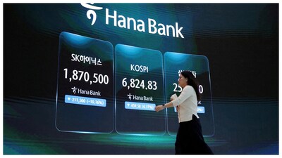 A currency dealer walks in front of an electronic board displaying SK Hynix and Samsung Electronics stock prices and the Korea Composite Stock Price Index (KOSPI) at the dealing room of a bank in Seoul. (Courtesy: Reuters file photo)