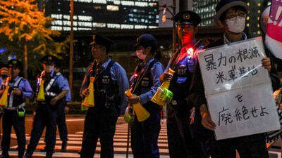 A demonstrator holds a placard that reads "Abolish U.S. military bases, the root of violence." as police officers stand guard during a protest outside the Prime Minister's office following the killing of a Japanese woman in Okinawa, for which a US Marine is a suspect, in Tokyo, Japan, October 5, 2026.  REUTERS/Kim Kyung-Hoon